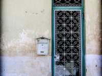 a metal door in turquoise with many white ornaments in the front of an old house in aegio in achaia