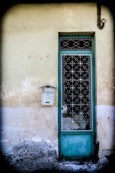 a metal door in turquoise with many white ornaments in the front of an old house in aegio in achaia
