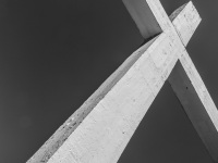 the big cross at the memorial of kalavrita with the top of a cypress and a very small clowd, black-and-white