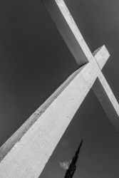 the big cross at the memorial of kalavrita with the top of a cypress and a very small clowd, black-and-white
