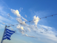 a greek flag and fairy lights under a blue sky with milky white clowds on a blue star ferry on the way to greece