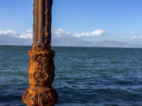 a by the sun illuminated rosty lamppost stands in front of the blue gulf of corinth