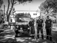three firefighters are posing in front of their car for the photo in the middle of the street in eleousa on rhodes, black-and-white