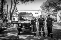 three firefighters are posing in front of their car for the photo in the middle of the street in eleousa on rhodes, black-and-white
