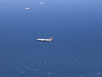 with the aegean sea in the background there are two ferries, one airplane and many surfer in the distance