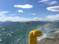 at the shore in nafplio you see a yello harbor poller, splashing water of the sea and the fort bourtzi in the background