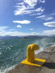 at the shore in nafplio you see a yello harbor poller, splashing water of the sea and the fort bourtzi in the background