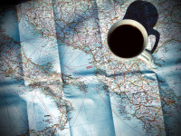 a shadow casting cup of black coffee stands on a map of italy and greece for planing a roadtrip