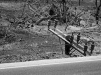 the electrical cross arms of a burned electricity pole are laying on the ground next to the street in kiotari on rhodes at the fire in 2023, black-and-white