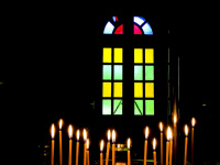 burning candles in front of a colorful church window in the dark church of the dormition of the virgin in kalavrita
