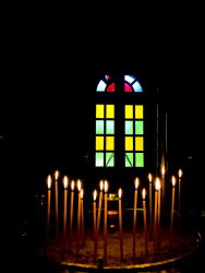 burning candles in front of a colorful church window in the dark church of the dormition of the virgin in kalavrita