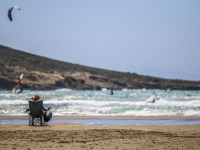 woman on a folding beach chair is watching kitesurfer in the waves of the sea in prasonisi on rhodes