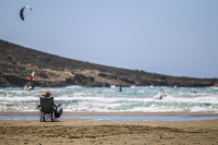woman on a folding beach chair is watching kitesurfer in the waves of the sea in prasonisi on rhodes