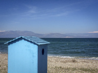 a changing room in form of a light blue wooden cottage stands at the beach in diakopto at the gulf of corinth