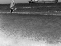from splashin waves at the beach in prasonisi you see a surfer and to a tanker in the background, black-and-white