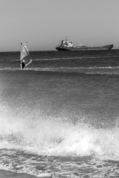 from splashin waves at the beach in prasonisi you see a surfer and to a tanker in the background, black-and-white