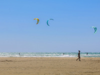 a woman is walking at the beach in prasonisi on rhodes and pasts kitesurfers there