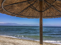a straw parasol at the beach in diakopto with a view to the gulf of corinth