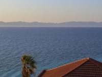 a red tiled roof and a palm are standing in front of the aegean sea in monte smith on rhodes at an evening light