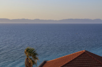 a red tiled roof and a palm are standing in front of the aegean sea in monte smith on rhodes at an evening light
