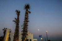 two palms, an oriental house and lanterns are standing in front of a sunset sky with a little white moon at elli beach in rhodes city