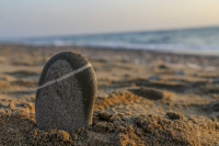an upright grey stone in the sandy limni beach on rhodes with the ocean behind and sunsetlight
