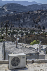 an air conditioner on top of houses in asklipio on rhodes are standing in front of the burned landscape around the village