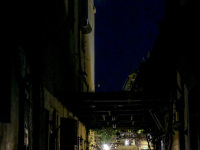 through a dark alley in the old town of rhodes you see the light and guests at chairs of a restaurant