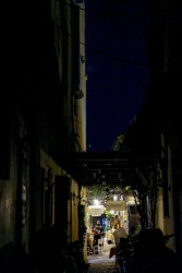 through a dark alley in the old town of rhodes you see the light and guests at chairs of a restaurant