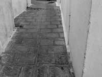 at the end of a smcall alley in the village lindos on rhodes is standing a motocycle, black-and-white