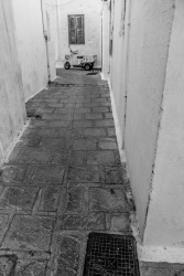 at the end of a smcall alley in the village lindos on rhodes is standing a motocycle, black-and-white