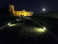 a path with cobblestones is leading to the castello di bovino in puglia by night