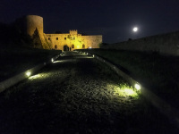 a path with cobblestones is leading to the castello di bovino in puglia by night
