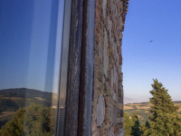 the blue sky, the landscape around bovino in puglia and the stone wall of the residenza ducale are reflecting in a window of the hotel