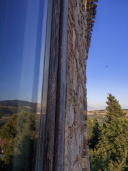 the blue sky, the landscape around bovino in puglia and the stone wall of the residenza ducale are reflecting in a window of the hotel