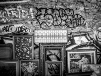 on a stone wall full of graffiti in monastiraki in athens are leaning diverse pictures in frames, black-and-white