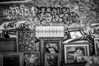 on a stone wall full of graffiti in monastiraki in athens are leaning diverse pictures in frames, black-and-white