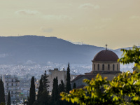 a tree and a greek orthodox church in front of the city athens in a nice evening light