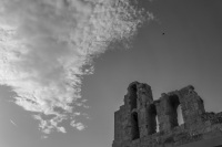 a bee, a plane, funny clowds and the top of the herodes atticus theatre in athens in front of a bright sky, black-and-white