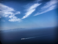 blue mediterranean sea with a little ferry, the blue sky and some clowds