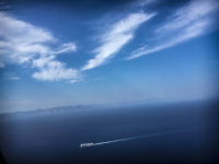 blue mediterranean sea with a little ferry, the blue sky and some clowds