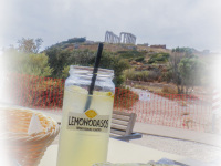 behind a greek salad with feta and a lemonade you see in the distance the columns of kap sounion in the south of attika