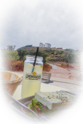 behind a greek salad with feta and a lemonade you see in the distance the columns of kap sounion in the south of attika