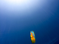 a colorful kite in prasonisi on rhodes at a dark blue sky, the sun is shining white over the scene