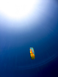 a colorful kite in prasonisi on rhodes at a dark blue sky, the sun is shining white over the scene