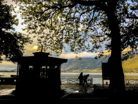 in front of the colorful lake pamvotida in ioannina you see trees, walker and a periptero in black like a silhouette