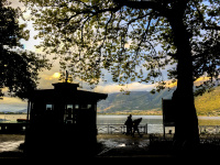 in front of the colorful lake pamvotida in ioannina you see trees, walker and a periptero in black like a silhouette