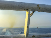 view from a shiprailing on the blue sea between greek mainland and the islands, a container ship and wake
