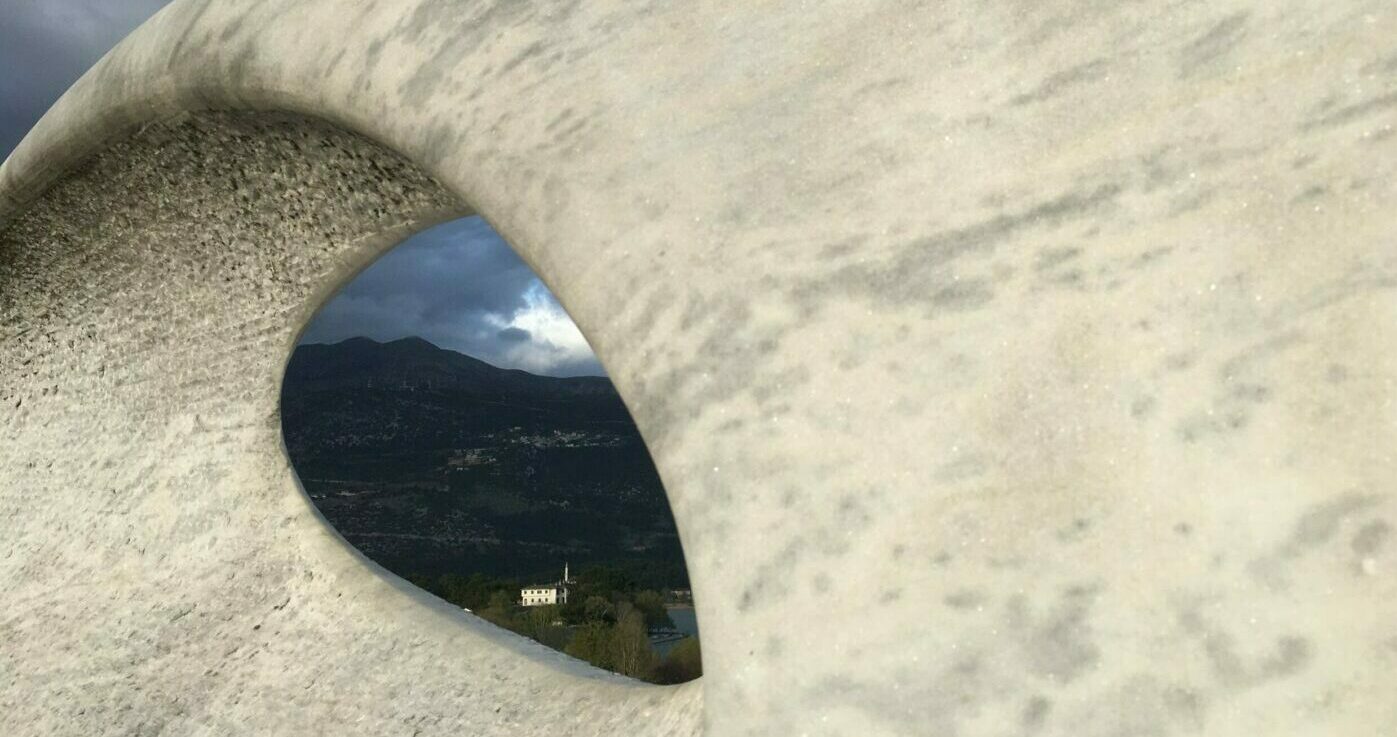 Blick durch eine graue Skulptur auf eine Moschee in einer griechischen Berglandschaft. Es erinnert an das Auge eines Aliens. FOTO MAU – Reisefotografie & mehr