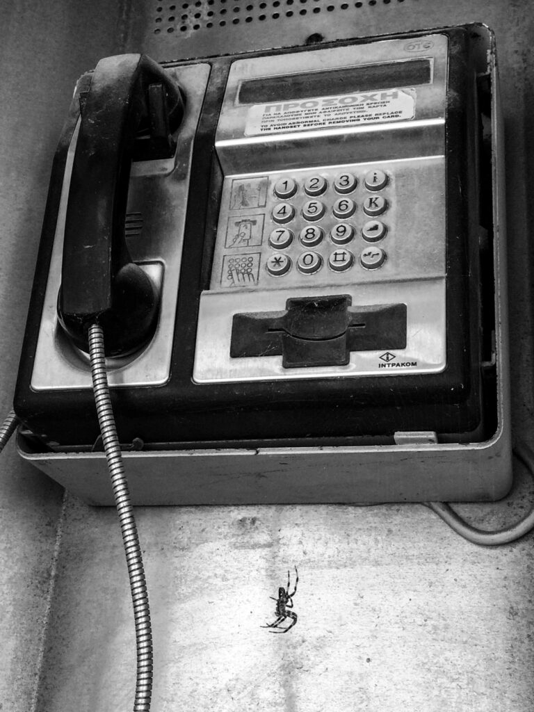 FOTO MAU kontaktieren Ein altes Telefon in einer griechischen Telefonzelle, scheinbar nicht mehr funktionstüchtig. Unten seilt sich eine große Spinne vom Telefon ab.